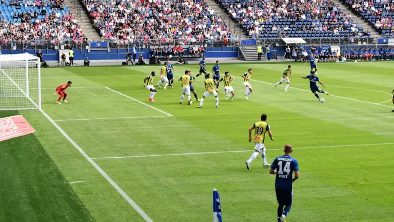 Jalgpallimängijad staadionil rohelisel muruväljakul, võistlusolukord täis tribüünidega taustal.