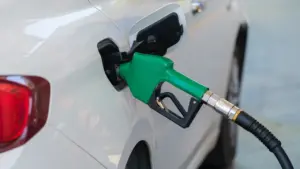 Kütusepüstol tankimas valget sõiduautot bensiinijaamas, keskendudes säästlikule tankimisele aastal 2026.