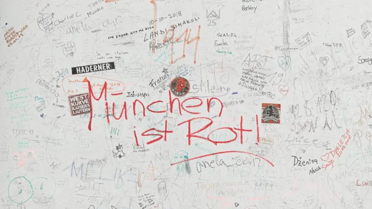 Müncheni teemaline grafiti valgel seinal, mis meenutab ajaloolist linna ja selle keerulist minevikku.