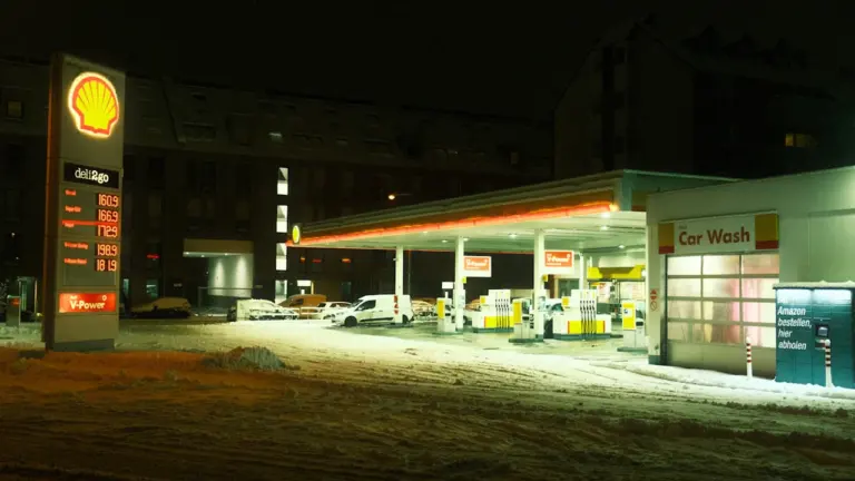 Öine tankla lumisel maastikul, kus on näha kütusehinnad infostendil.