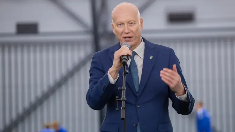 Kiilaspäine mees sinises ülikonnas kõneleb mikrofoni ees heledas ja avaras siseruumis.
